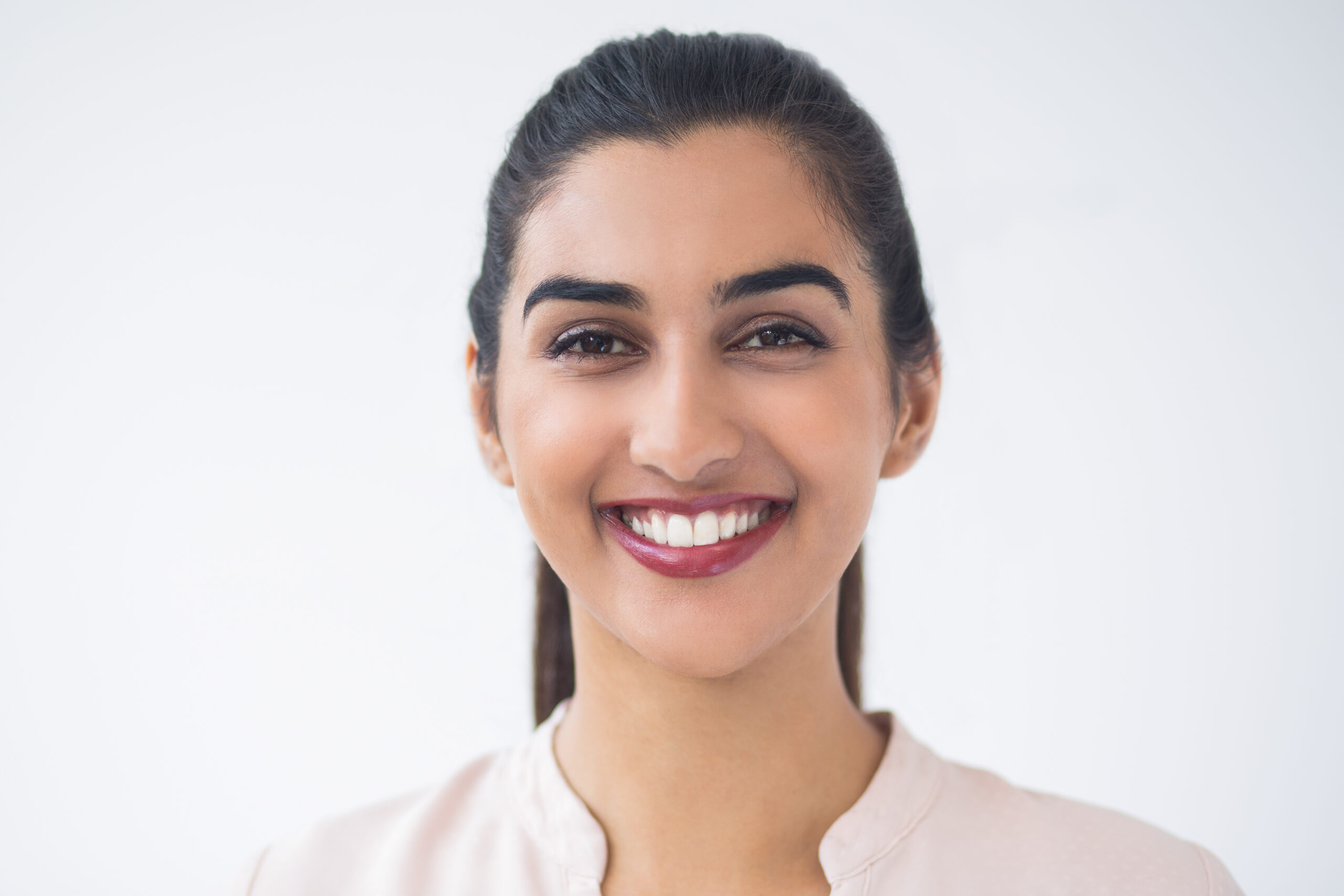Closeup portrait of smiling young beautiful Indian woman looking at camera. Isolated view on white background.